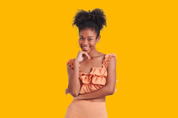 Beautiful african american girl with wear orange shirt dress an afro hairstyle smiling charming isolated yellow color background