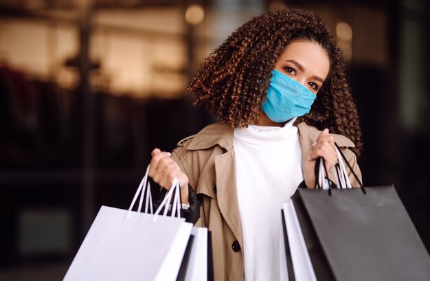 Beautiful african american woman in protective mask after shopping near the store