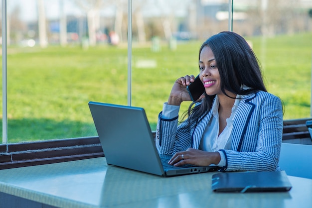 Beautiful African-American woman using a laptop and talking on her cell phone