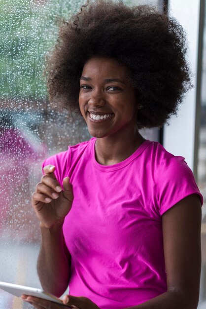 beautiful african american woman using tablet computer from home while rain and bad weather is outdoor