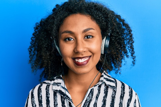 Beautiful african american woman with afro hair wearing call center agent headset looking positive and happy standing and smiling with a confident smile showing teeth