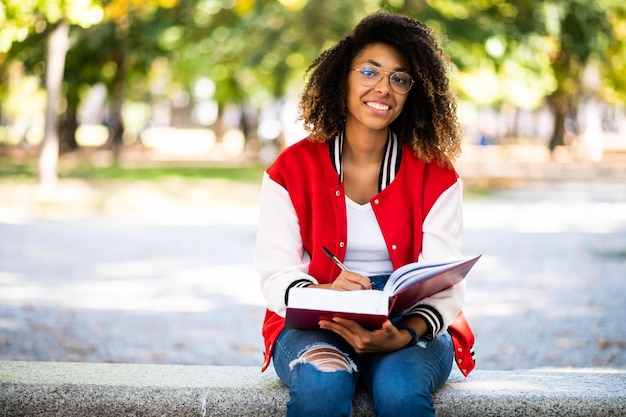 Beautiful african female college student reading a book on a bench in a park