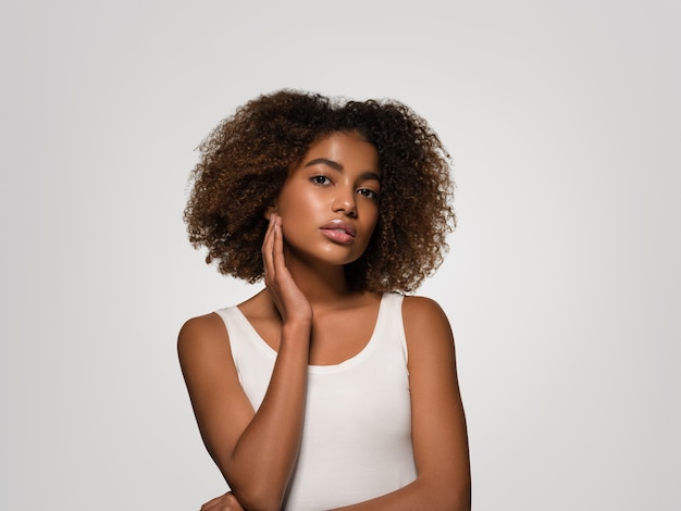 Beautiful african woman white t-shirt portrait afro haircut touching her face Color background gray