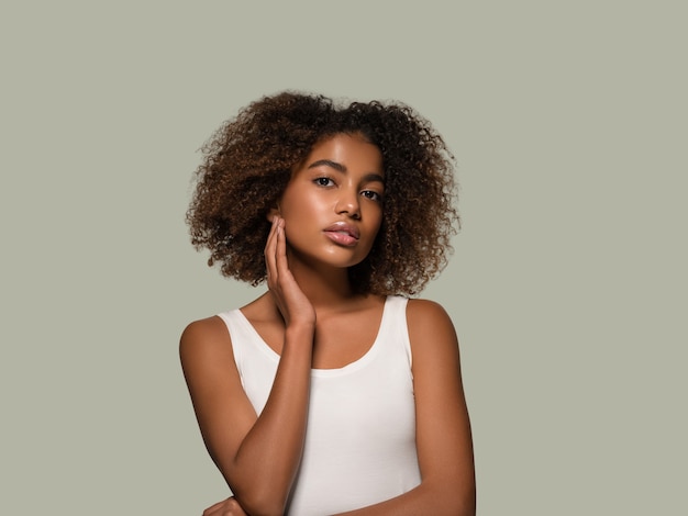 Beautiful african woman white t-shirt portrait afro haircut touching her face Color background green