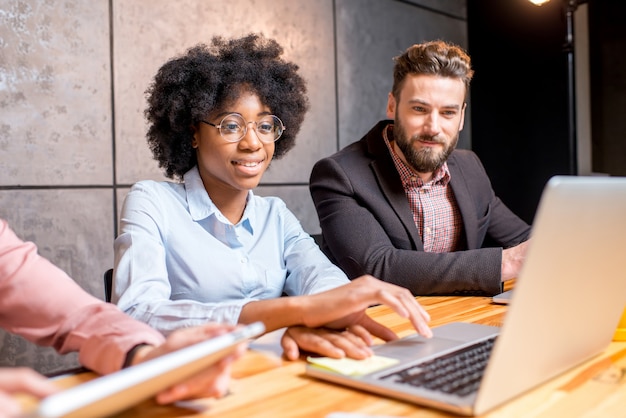 Beautiful african woman with handsome caucasian man working with laptop at the modern office interior