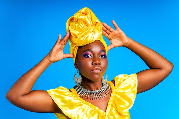 Beautiful african woman in yellow silk turban on head and dress with silver neckless and earrings nose piercing in blue studio background