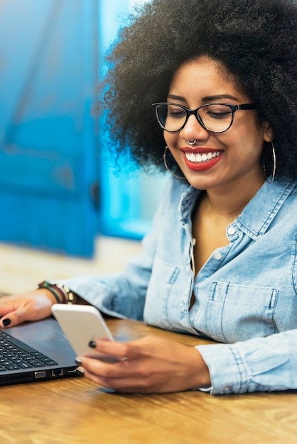 Beautiful afro american woman using mobile and laptop in the coffee shop. Communication concept.