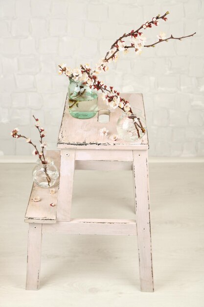 Beautiful apricot blossom in transparent jars on grey wall background