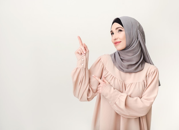 Beautiful arab woman pointing on copy space, studio portrait at white background