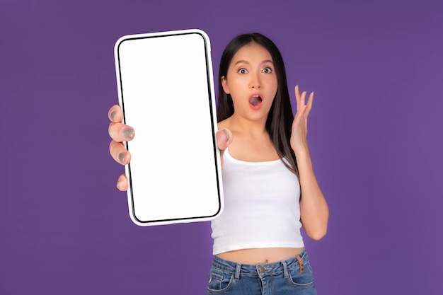 Beautiful Asian brunette woman cute girl in white tank top Excited surprised girl showing big smart phone with blank screen white screen isolated purple background Mock Up Image