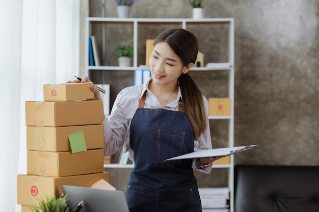 A beautiful Asian business owner opens an online store she is checking orders from customers sending goods through a courier company concept of a woman opening an online business