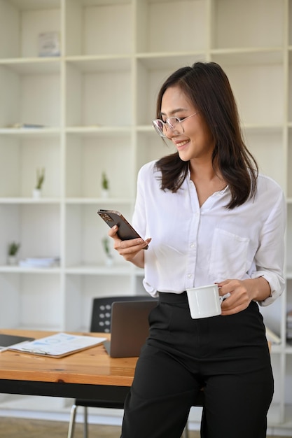 Beautiful Asian businesswoman standing in her office using her smartphone