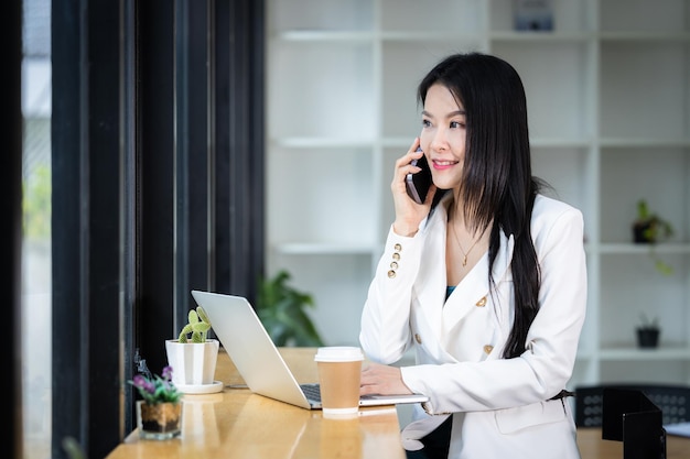 Beautiful asian businesswoman use smartphone and computer notebook laptop Business woman use mobile phone