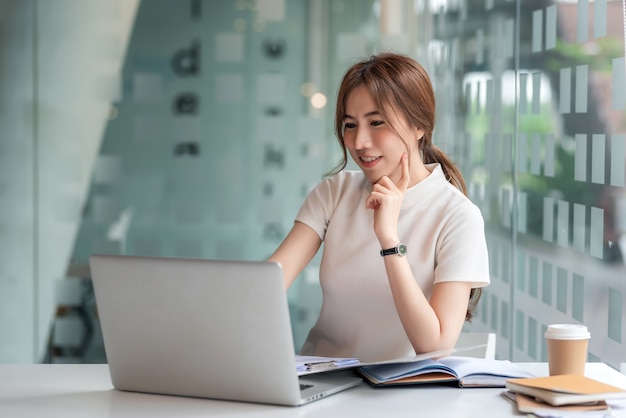 Beautiful Asian businesswoman working on a  laptop and documents at a modern office.