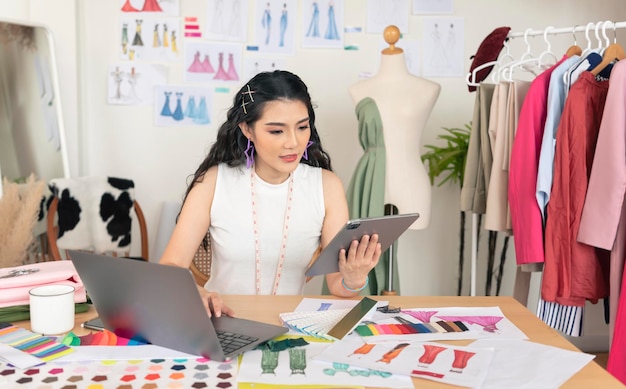 Beautiful asian Fashion designer drawing sketches for new collection on computer laptop