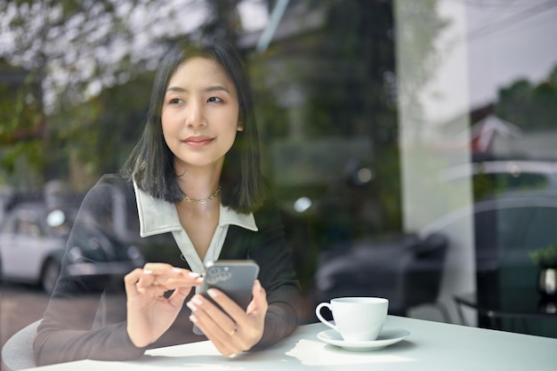 Beautiful Asian female in casual clothes using her phone in the coffee shop