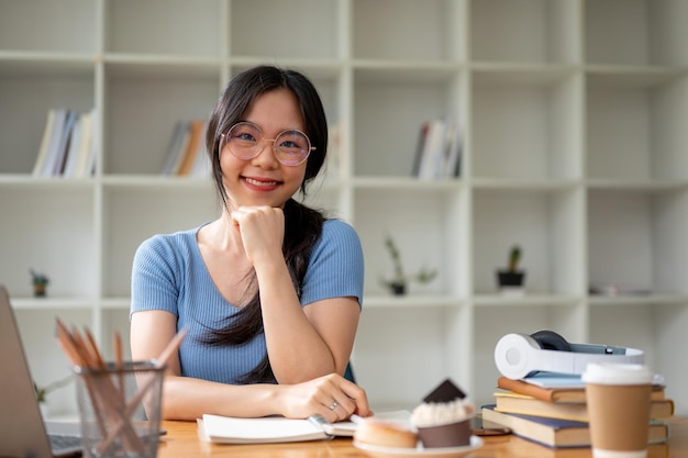 A beautiful Asian female college student in glasses sits at her study table at home