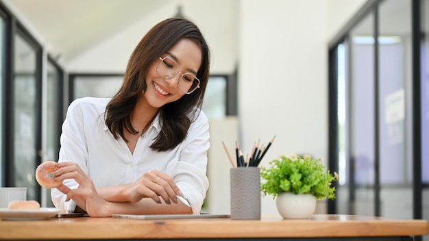 Beautiful Asian female office worker at her office desk reading an online content on tablet