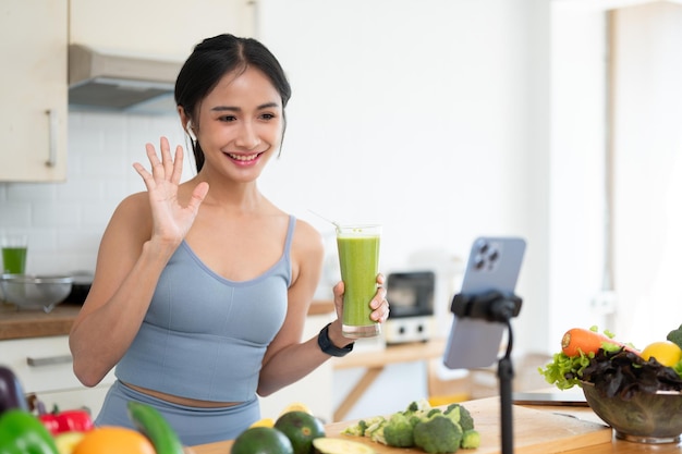 A beautiful Asian female online nutrition coach is live streaming while making her morning smoothie