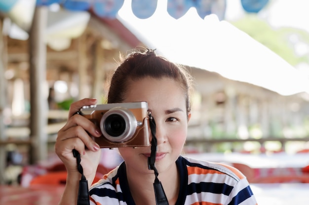 A beautiful Asian female photographer is raising a digital camera attached to the right eye to record images.