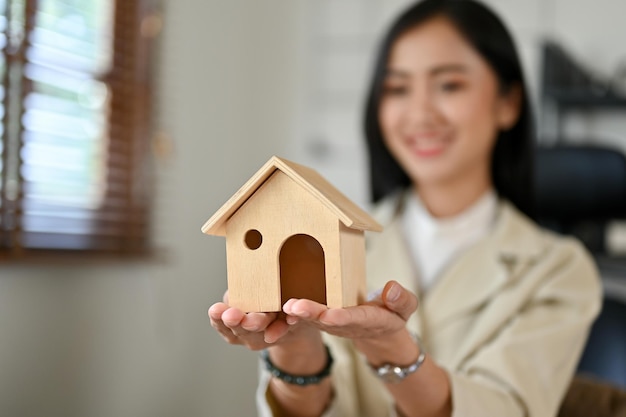 A beautiful Asian female real estate agent or realtor holding a house model Closeup