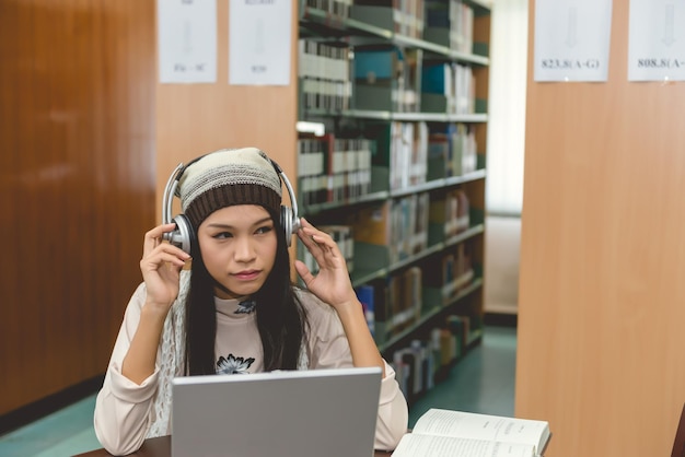 Beautiful asian female student listen song with laptop in the library