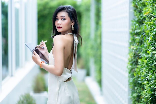 Beautiful asian freelance Success people business woman fashion model in summer white sleeveless dress using casual working with tablet for browsing internet chatting and blogging in coffee shop