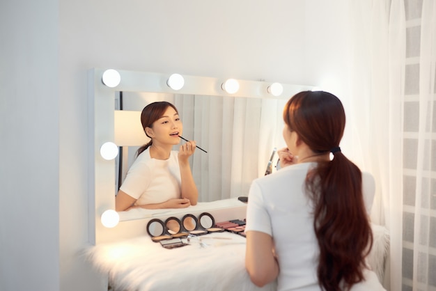 Beautiful Asian girl applying lipstick in front of mirror. Make up concept