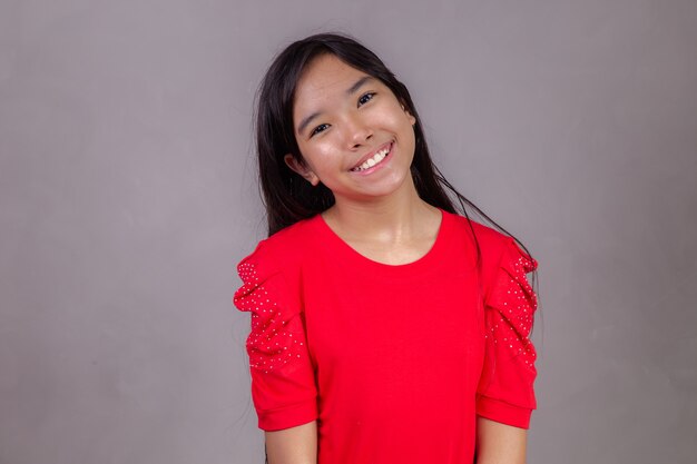 Beautiful asian girl sitting on grey background. Happy little Asian girl smiling.