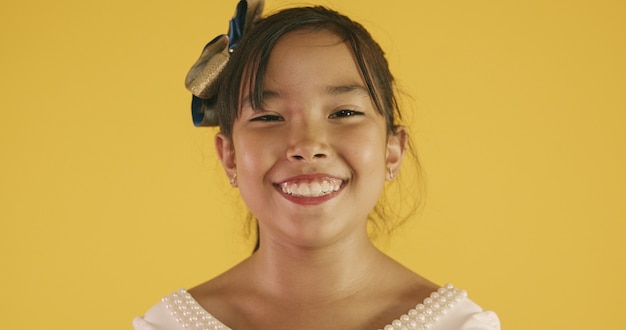 Beautiful asian girl sitting on yellow background. Happy little Asian girl smiling.