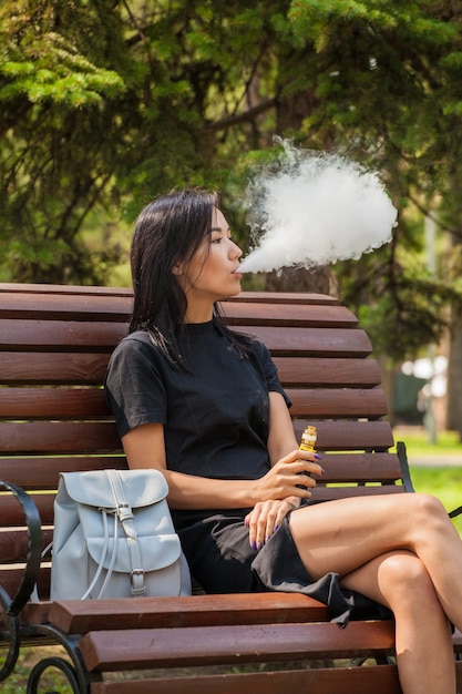 A beautiful Asian girl smokes a vape in a public place. The harm of smoking