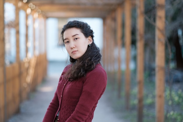 A beautiful Asian girl stands in modest clothes in the middle of an alley in the park