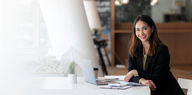 Beautiful asian indian businesswoman sitting at office desk smiling and looking at camera