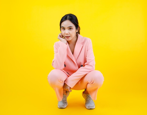 Beautiful Asian lady on gorgeous pink suit squatting with hand on chin and expressing attractive eye looking and calm thinking. Cute woman model posing with business cloth fashion and fascination.