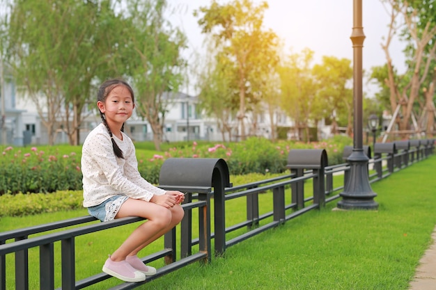 Beautiful Asian little girl child sitting in the garden on fence at public park outdoor