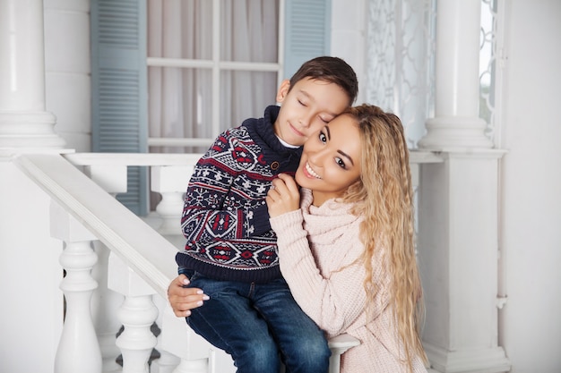 Beautiful asian  mother hugging with her little son on the white front porch of a country vacation house. 