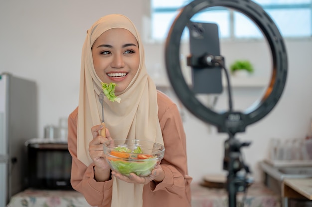 A beautiful Asian Muslim female food blogger is in the kitchen live streaming her food recipes