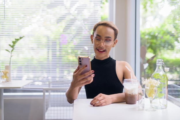 Beautiful Asian queer LGBT community supporter man using mobile phone in coffee shop