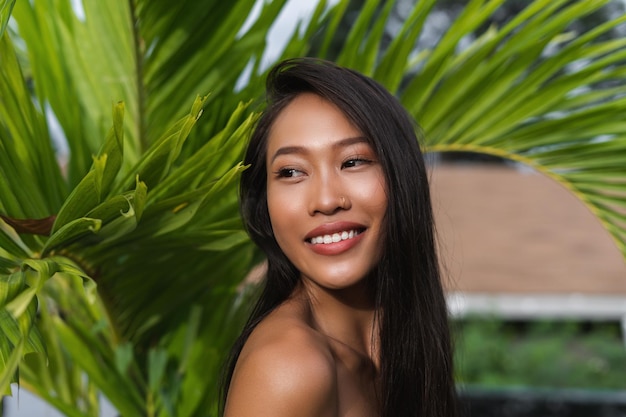 Beautiful asian thai woman with soft smooth clean dark tanned skin beauty portrait skincare positive posing with green leaves plump lips outdoor natural beauty