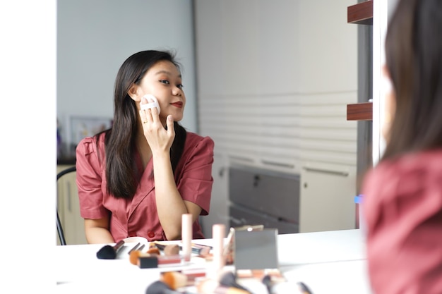 Beautiful Asian woman doing makeup in front of a dressing table mirror