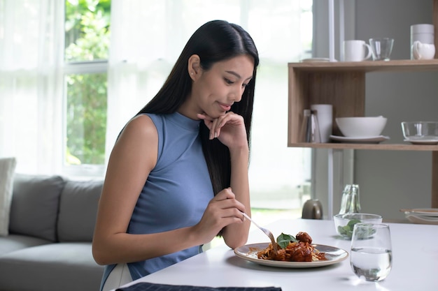 Beautiful Asian woman eating pasta on table in the morning at home Smiling healthy woman eating spaghetti while sitting and having breakfast at the kitchen table