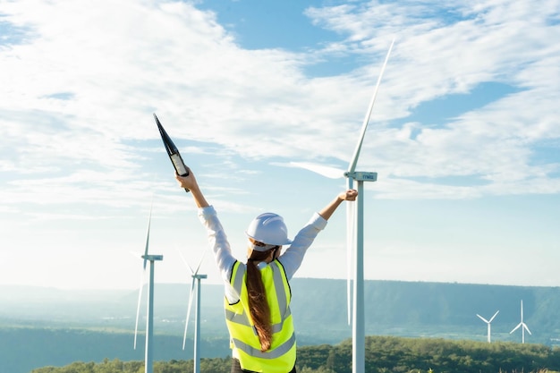 Beautiful Asian woman Engineer in white helmet working with document at renewable energy farm Female inspector controlling functioning of wind turbines Enery sustainable generatorelectricity