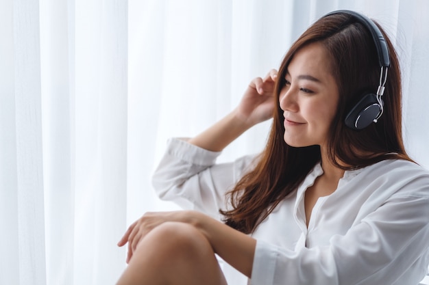 A beautiful asian woman enjoy listening to music with headphone in bedroom , happiness and relaxation concepts