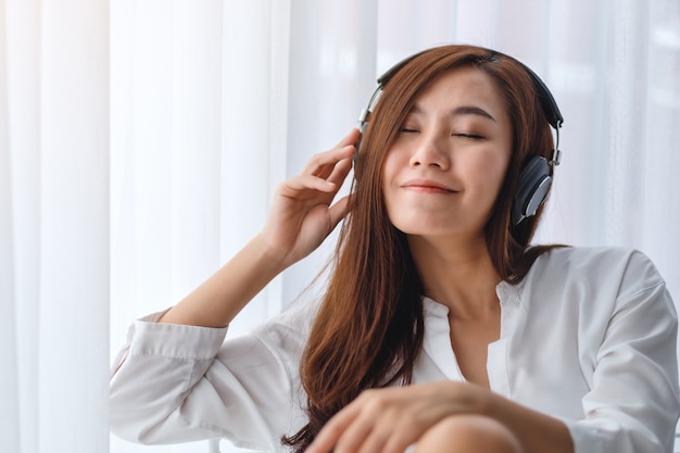 A beautiful asian woman enjoy listening to music with headphone in bedroom