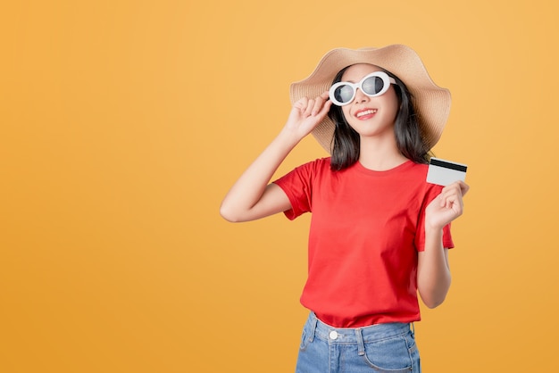 Beautiful Asian woman good skin, wearing sunglasses posing holding credit card payment on orange .