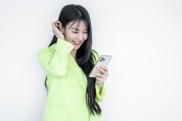 Beautiful Asian woman in green suit pastel holding smart phone and smiling isolated on white background Happy joyful girl with celebrating victory Asian woman successful happiness