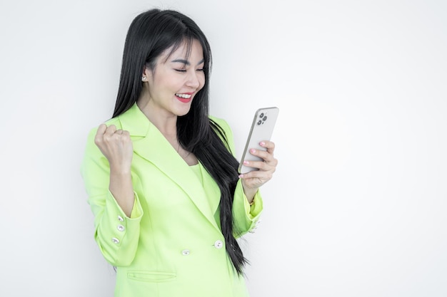 Beautiful Asian woman in green suit pastel using smart phone gesturing yes isolated on white background Happy joyful girl with long hair celebrating victory asian woman successful social media