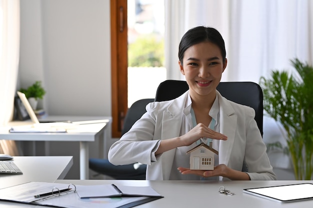 Beautiful asian woman hands protecting house model. Insurance or loan real estate concept.