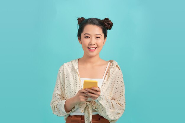 Beautiful Asian woman holding smartphone and smiling on blue background