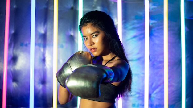 Beautiful Asian Woman is training and punching with Silver gold Mitts Gloves. Office Girl exercises in Modern color Neon Muay Thai Boxing Gym with sweat water splash